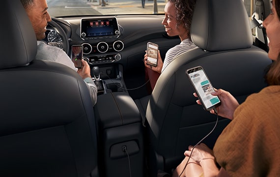 2022 Nissan Sentra 內飾，乘客在使用智能手機，展示設備連通性。
