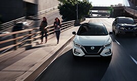 2023 Nissan Sentra 白色四門轎車前視圖，行駛在城市街道上。